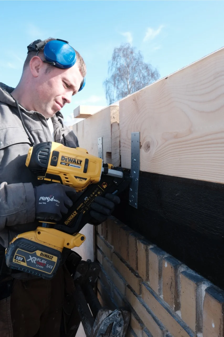 A construction worker fastening timber above a brick wall